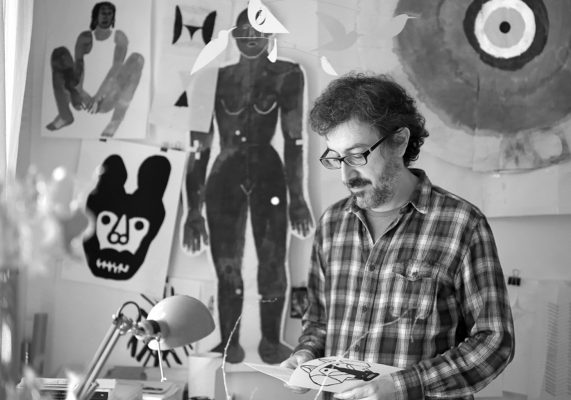 Jesus Cisneros Six/Seis publication. Image of Jesus in his studio looking at sketchbooks.